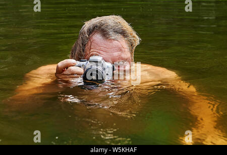 Homme mature fait du voyeurisme à la surface de l'eau de la rivière avec l'aide de l'appareil photo imperméable dans ses mains. Banque D'Images