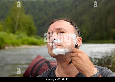 Rasoir avec l'homme blanc dans sa main est son visage rasage, couverts par de la mousse, dans la nature sauvage, l'éco-tourisme. Banque D'Images