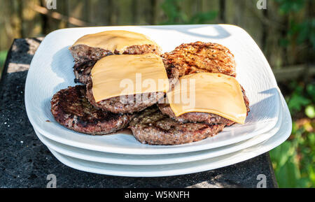 Hamburgers et cheeseburgers grillés juste sur une plaque blanche à un bbq familial.. Banque D'Images