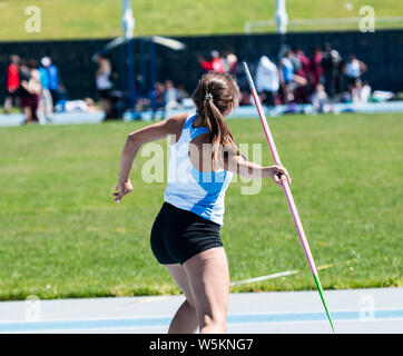 Une vue arrière d'une lycéenne de lancer un javelot rose sur une pelouse au cours d'une compétition d'athlétisme. Banque D'Images