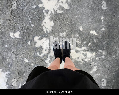 Pieds et Jambes vu de dessus. Pieds de selfies dans mode sneakers noir sur fond des chaussées, vue du dessus. Belle femme chaussures noires debout sur conc Banque D'Images