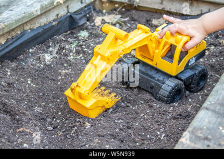 La main d'un enfant pousse un jouet le long de l'excavateur dans un jardin en boîte Banque D'Images