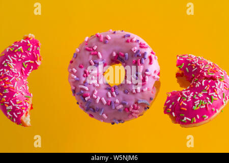 Rose lumineux des beignets sucrés avec sprinkles sur fond jaune dynamique Banque D'Images