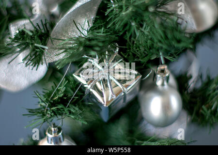 Jouet de l'arbre de Noël sous la forme d'une boîte d'argent accroché sur les branches d'un arbre de Noël artificiel Banque D'Images