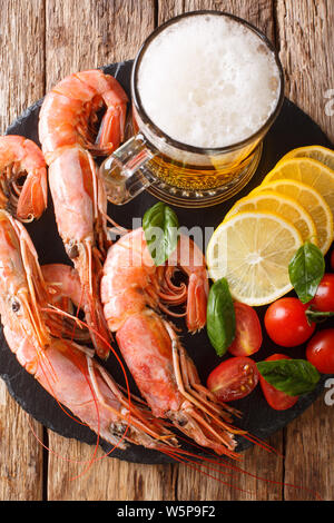 La bière mousseuse avec de délicieuses crevettes, citron et tomates sur une liste de sélection sur la table. Haut Vertical Vue de dessus Banque D'Images