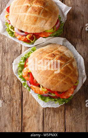 Pita aux crevettes, tomates, poivrons, oignons et salade close-up sur le parchemin sur la table. Haut Vertical Vue de dessus Banque D'Images