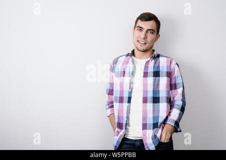 Portrait de jeune homme moderne de l'Europe en chemise à carreaux rose et blanc T-shirt contre le mur gris with copy space Banque D'Images