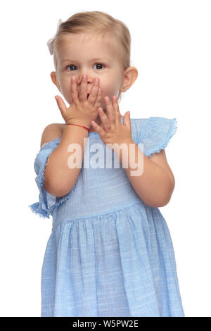 Smiling little girl couvrant sa bouche avec une main, prêt à envoyer un baiser sur fond blanc Banque D'Images