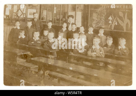 Carte postale édouardienne des écoliers en classe, carte de l'Irlande, tulipe et chute de neige sur le tableau noir, maîtresse stricte de l'école en arrière-plan, éventuellement St Michaels C E école primaire, Howe Bridge, Manchester Royaume-Uni vers 1906 Banque D'Images