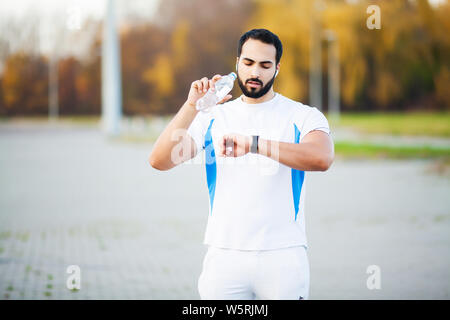 Épuisé runner homme boire de l'eau sur le parc après entraînement Banque D'Images