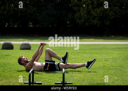 Man performing réchauffer avant de faire la gymnastique fitness workout dans un parc public en plein air, UK Banque D'Images