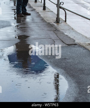 Lyme Regis, dans le Dorset, UK. 30 juillet 2019. Météo France : Après des jours de soleil, de fortes averses de pluie a frappé la station balnéaire de Lyme Regis marquant une pause à la vague de chaleur du mois de juillet. Un homme s'abrite de la pluie sous un parapluie bleu comme une autre douche pluie hits le front Crédit : Celia McMahon/Alamy Live News. Banque D'Images