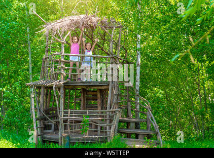 Deux petites filles heureux dans une maison de l'arbre en bois sur une journée ensoleillée. Les soeurs se réjouissent de l'été. Le concept de l'été. Le soleil brille. Banque D'Images