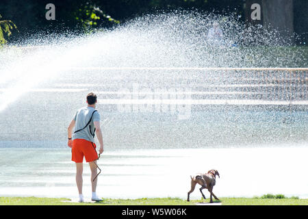 29/07/2019. Battersea, Londres, Royaume-Uni. Un homme jette un bâton pour son chien à côté de l'eau des fontaines dans Battersea Park sur une chaude journée ensoleillée. Banque D'Images