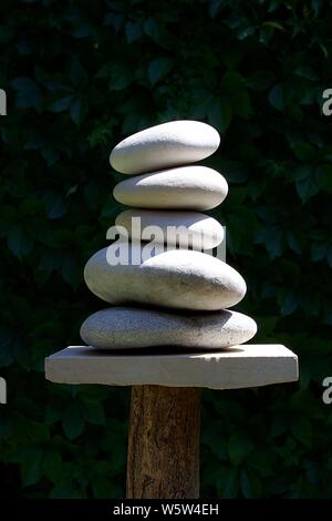Sculpture zen de cinq cailloux blancs cairn tour a marbre et d'une connexion. Arrière-plan flou de feuillage vert foncé Banque D'Images
