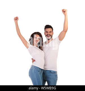 Casual couple heureux des succès à célébrer avec les mains en l'air sur fond blanc Banque D'Images