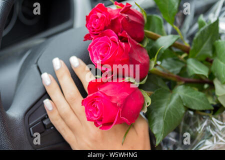 Dans la voiture dans les mains d'une femelle pond un bouquet de roses roses sur le guidon Banque D'Images