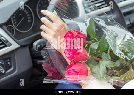 Dans la voiture dans les mains d'une femelle pond un bouquet de roses roses sur le guidon Banque D'Images