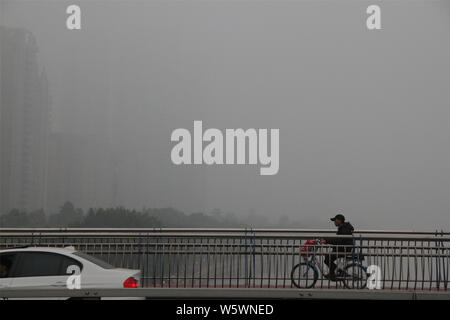 --FILE--un cycliste portant un masque contre la pollution de l'air promenades dans le smog lourd dans la ville de Guangzhou, province du Guangdong en Chine du Sud, 3 mars 2014. T Banque D'Images