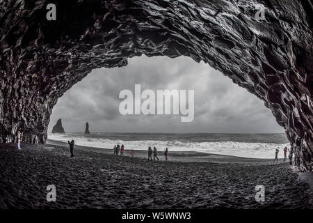 Les touristes à la découverte de rares formations grotte rocheuse dans la plage de sable noir, l'Islande Banque D'Images