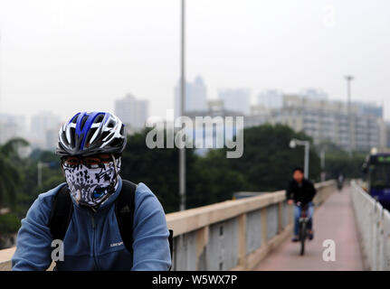 --FILE--un cycliste portant un masque contre la pollution de l'air promenades dans le smog lourd dans la ville de Guangzhou, province du Guangdong en Chine du sud, le 11 décembre 2013. Banque D'Images