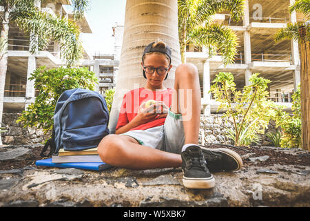 Heureux l'étudiant à prendre une pause d'études et de manger un fruit collation santé après l'école sous des arbres. Jeune garçon faisant des repas Petit déjeuner dans la nature de la jeunesse li Banque D'Images