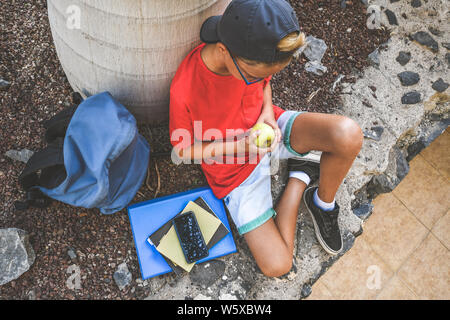 Heureux l'étudiant à prendre une pause d'études et de manger un fruit collation santé après l'école sous des arbres. Jeune garçon faisant des repas Petit déjeuner dans la nature de la jeunesse li Banque D'Images