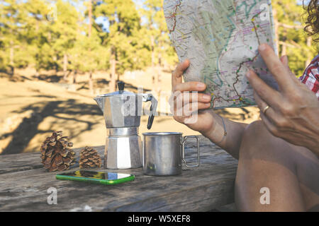 Vue rapprochée de femme mains tenant un site piscine en plein air dans le parc. Cafetière, mug, smartphone et des pommes de pin sur une table en bois de montagne Aventure Banque D'Images