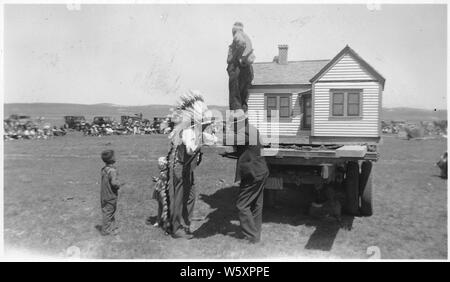 Vendeur et l'Indien à la maison modèle à l'échelle sur l'arrière d'un camion. Ville de Oglala. ; la portée et contenu : indien avec war bonnet plein de négocier avec le vendeur ; petit garçon admire la chambre. Banque D'Images