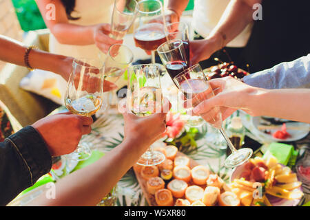 Des mains avec des verres de vin rouge de trinquer à servi table. Banque D'Images