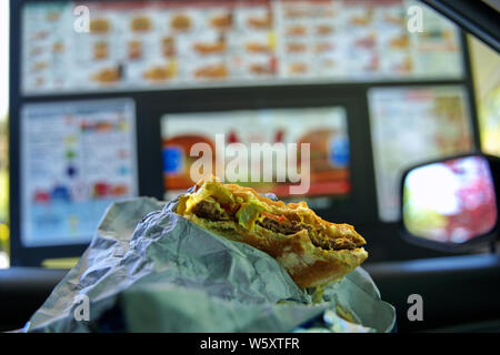 Mordu un cheeseburger dans les mains d'un pilote de la faim parqué par un lecteur numérique de kiosque. Banque D'Images