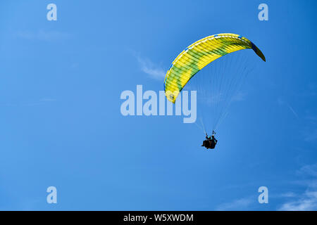 Un parapente en tandem et avec un parachute jaune et bleu et nuages de haute altitude. Banque D'Images