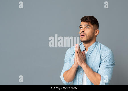 Hispanic Man Holding Hands en priant geste sur fond gris Banque D'Images