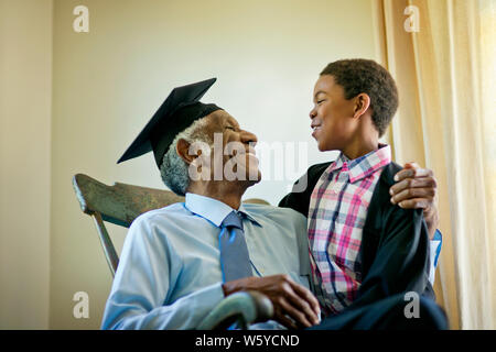 Hauts homme portant un mortier, assis dans un rocking-chair avec son petit-fils. Banque D'Images