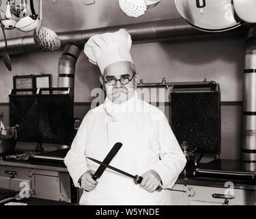 Années 1920 Années 1930 CHEF SÉRIEUX HOMME PORTANT TOQUE DEBOUT DANS cuisine professionnelle à la caméra au couteau d'affûtage sur l'acier - c8337 HAR001 HARS LA PEUR DE VIE CARRIÈRE EMPLOIS PERSONNES DEMI-LONGUEUR PROFESSION LES HOMMES D'ÂGE MOYEN DES EXPRESSIONS DE CONFIANCE B&W HOMME D'ÂGE MOYEN DE CONTACT AVEC LES YEUX DE L'OCCUPATION COMPÉTENCES MOUSTACHE MOUSTACHES COMPÉTENCES CONNAISSANCES CARRIÈRES STERN PUISSANT FIERS DE POUVOIR SUR LES CHEVEUX DU VISAGE ÉLÉGANT CRÉATIVITÉ DÉCOUPAGE CONCEPTUEL PROFESSIONS MID-ADULT MID-ADULT MAN d'affûtage de précision TOQUE NOIR ET BLANC DE L'ORIGINE ETHNIQUE CAUCASIENNE HAR001 old fashioned OLD SCHOOL DE GRAVES Banque D'Images