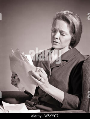 1960 WORRIED WOMAN HOLDING deux mains pleines DE PROJETS ET LES FACTURES EN TRAIN DE LIRE ET À LA RECHERCHE À TRÈS GRANDE QUANTITÉ DE DOCUMENTS - s15423 HAR001 LE HARS RETROUVEZ LE RÉSUMÉ DU PROBLÈME DE LA DETTE DE VIE FEMMES STUDIO SHOT MOODY ACCUEIL ESPACE COPIE DE LA VIE, mi-longueur CHERS PERSONNES EXPRESSIONS RISQUE B&W EN DIFFICULTÉ LA TRISTESSE DANS LES YEUX DES FEMMES AU FOYER ET À LA FEMME AU FOYER EN DÉTRESSE DE PRÉOCCUPATION de l'humeur morose échapper au foyer montant misérable faillite immense jeune adulte FEMME NOIR ET BLANC DE L'ORIGINE ETHNIQUE CAUCASIENNE HAR001 Factures old fashioned Banque D'Images