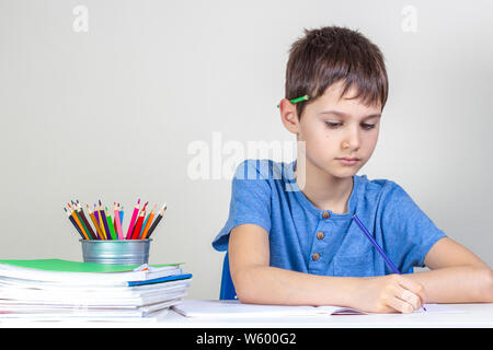 Kid fait ses devoirs à la table. L'accent garçon avec crayon derrière l'oreille écrit au crayon Banque D'Images