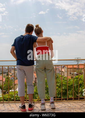 Le jeune homme et la jeune fille, enlacés, debout sur le balcon et regarder le paysage. La photo est prise à partir de l'arrière. Banque D'Images