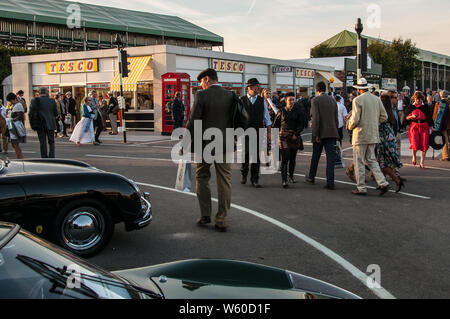 Scène de rue au Goodwood Revival avec des gens dans la période vestimentaire et voitures. Tesco store rétro. Costume d'époque. Scénario intemporel au crépuscule. Soir Banque D'Images