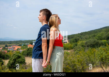 Une fille avec un T-shirt rouge et des cheveux blonds et un jeune homme dans un tee-shirt bleu sont debout avec le dos appuyé à l'autre sur la toile de fond Banque D'Images