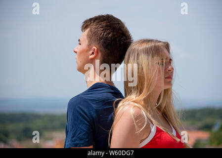 Une fille avec un T-shirt rouge et des cheveux blonds et un jeune homme dans un tee-shirt bleu sont debout avec le dos appuyé à l'autre sur la toile de fond Banque D'Images