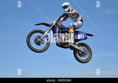 Un motard sur moto scramble, sauter haut dans le ciel bleu. Le motocross est une forme de course de moto qui a eu lieu sur des circuits hors-route. Dirt bike mx Banque D'Images