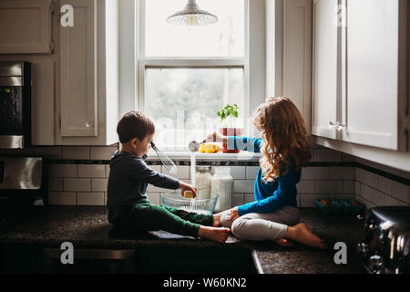 Jeune garçon et fille assise sur le comptoir de cuisine en mélangeant la pâte à muffins Banque D'Images