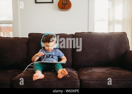Jeune garçon assis sur table à l'aide de tablet et portant des écouteurs Banque D'Images