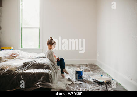 Jeune fille assise sur le lit dans la chambre fraîchement peint en blanc Banque D'Images