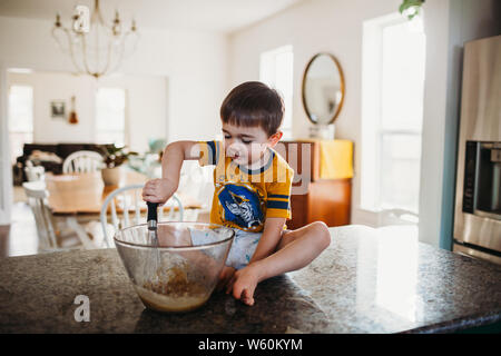 Jeune garçon assis sur le comptoir mixer avec wisk Banque D'Images