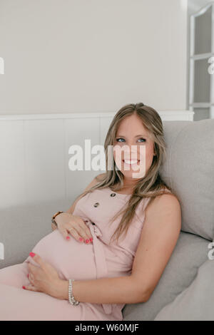 Cheerful pregnant woman sur le canapé touche son ventre Banque D'Images