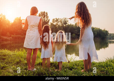 Balades Familiales d'été par river au coucher du soleil. Mère, grand-mère et enfants admirant le paysage après pique-nique. 3 denerations Banque D'Images
