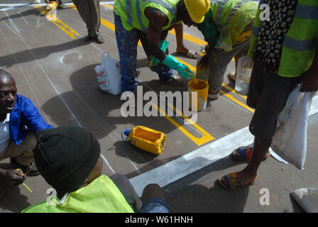 Repeindre les travailleurs de la route passage piétons bandes sur la surface de la route, Lilongwe, Malawi, Afrique. Banque D'Images