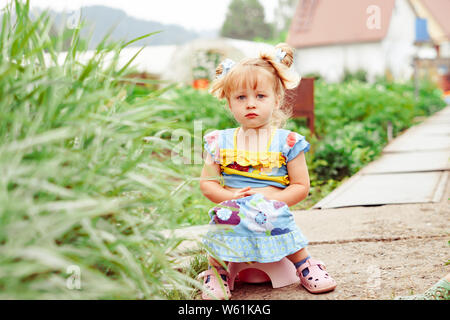 Portrait of cute little girl sitting on petit pot à l'extérieur Banque D'Images